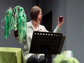 Picture of the artist workshopping 'Being Green and Other Mysteries,' shaking a tree and an apple